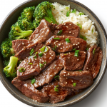 Beef and broccoli with white rice in a bowl, topped with sesame seeds and scallions.