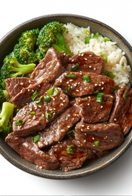 Beef and broccoli with white rice in a bowl, topped with sesame seeds and scallions.