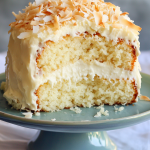 Moist coconut milk cake with creamy white frosting and toasted coconut flakes on a cake stand